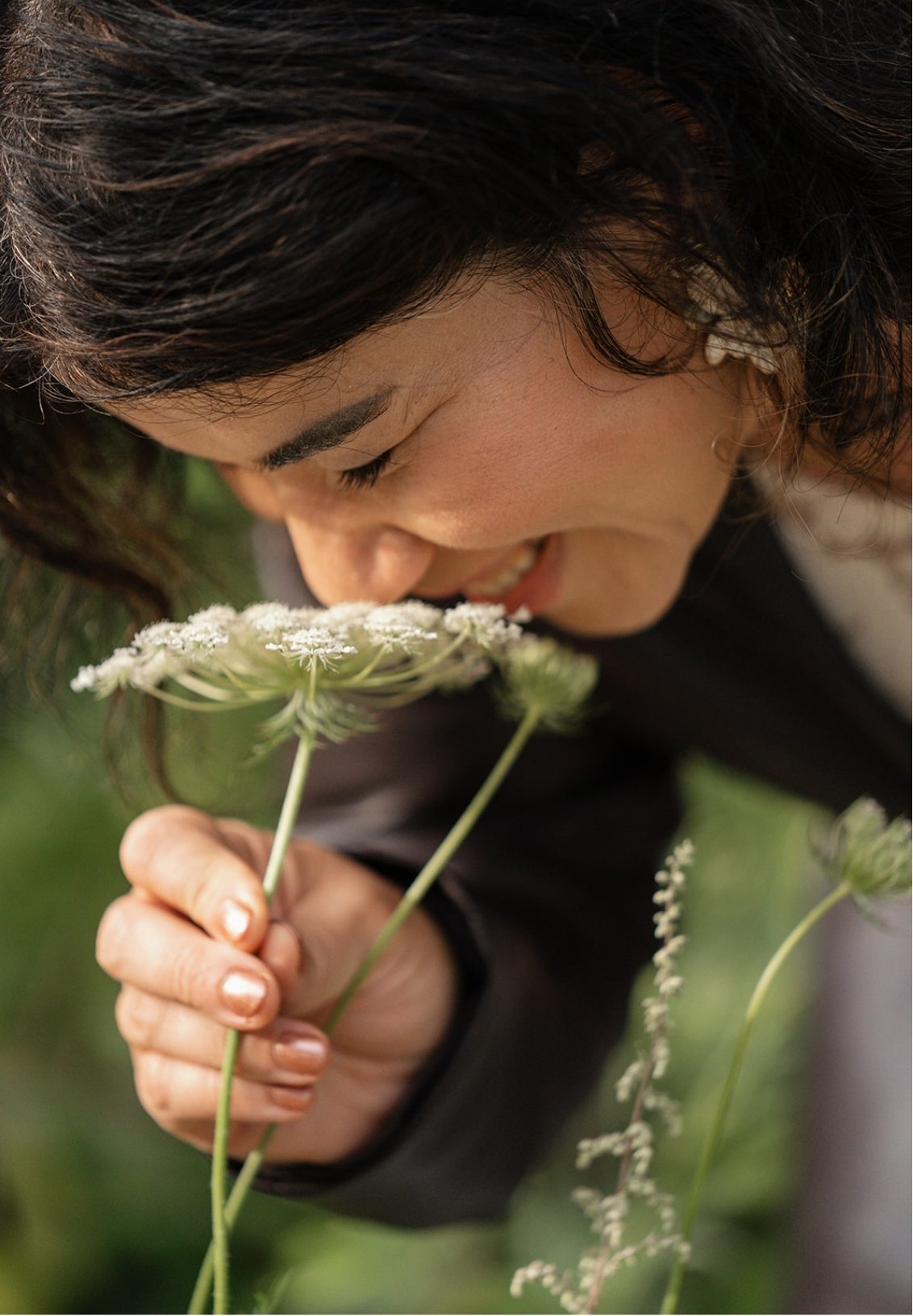 A woman smelling white flowers outdoors.