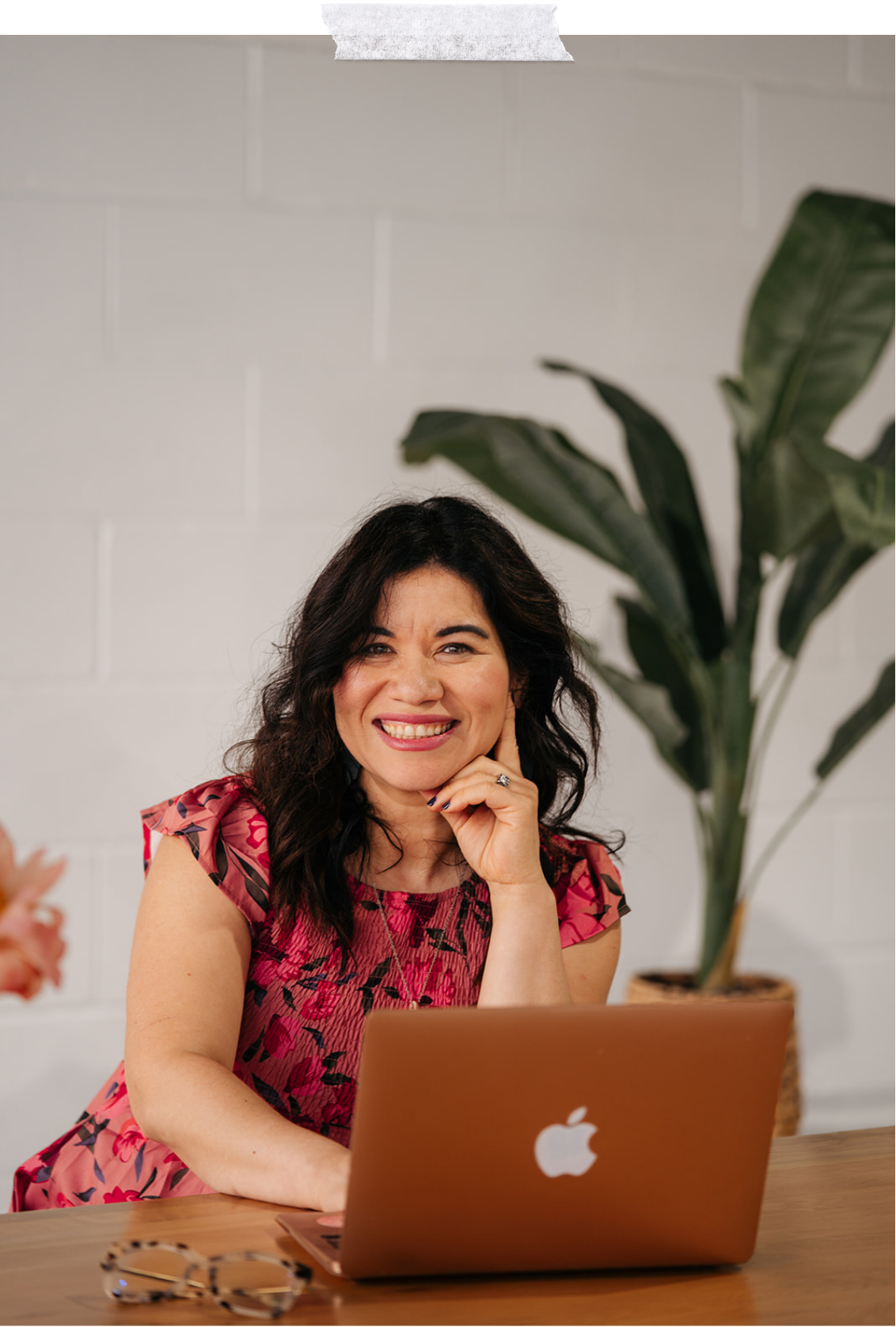 Adaris Pickett, Christian therapist in Boston, sitting at a wooden desk with a rose gold MacBook, smiling at the camera, with a large green plant in the background.