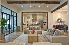 Open-concept living room with neutral tones, large windows, and modern furniture, leading into a kitchen and dining area.