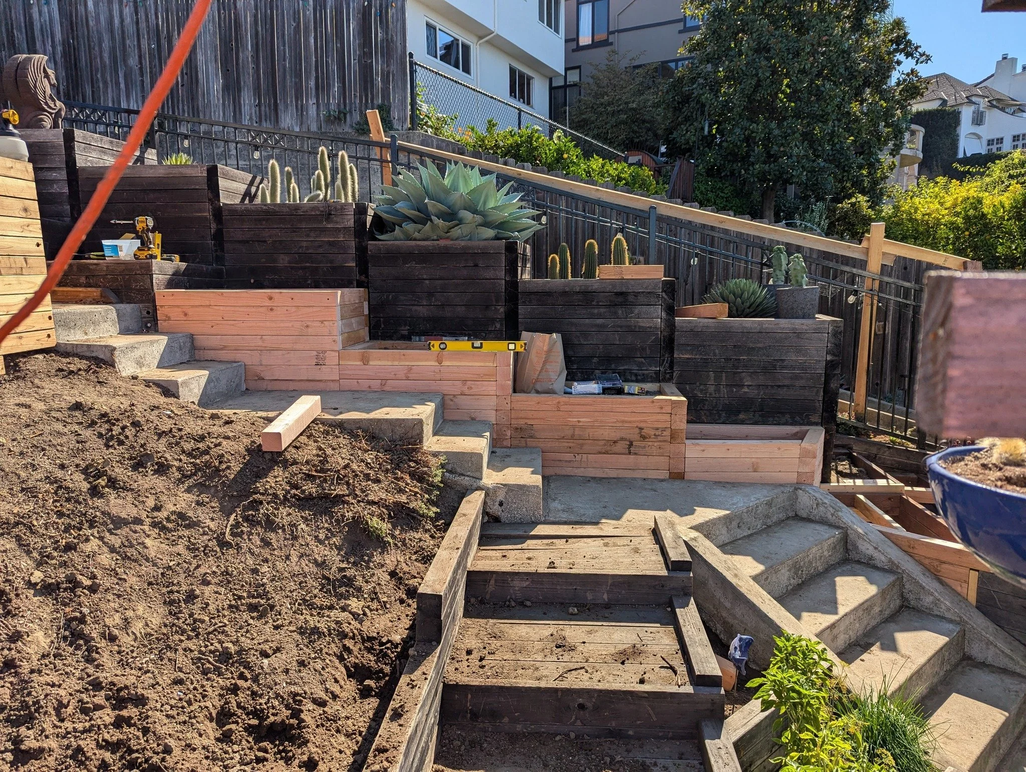 Construction of outdoor stairs and retaining walls with wooden planters and succulents in a backyard garden.