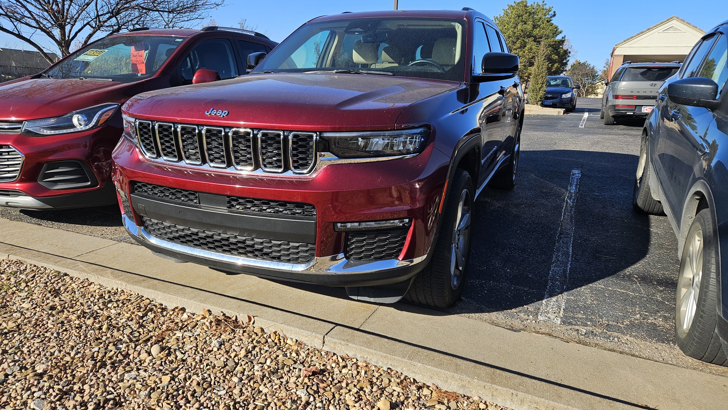 A maroon 2021 Jeep Grand Cherokee parked in a sunny lot, showcasing its signature seven-slot chrome grille and sleek LED headlights.