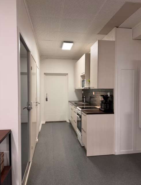 A small, modern kitchen with white cabinets, stainless steel appliances, a black backsplash, and a coffee maker on the countertop.