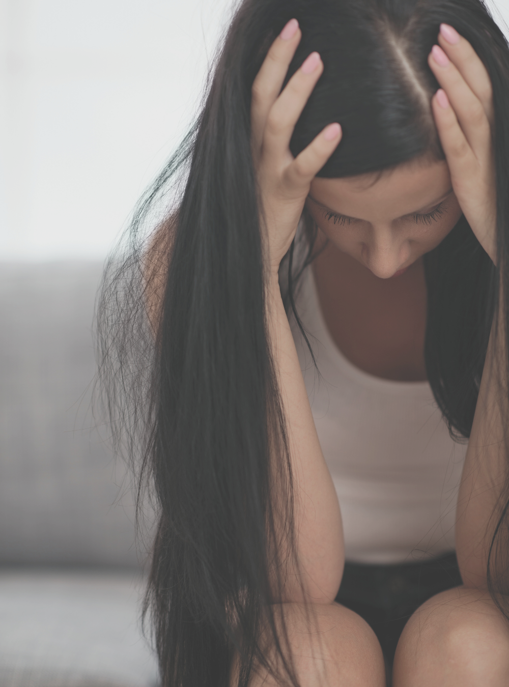 A woman with long dark hair holding her head with both hands, appearing distressed or upset.