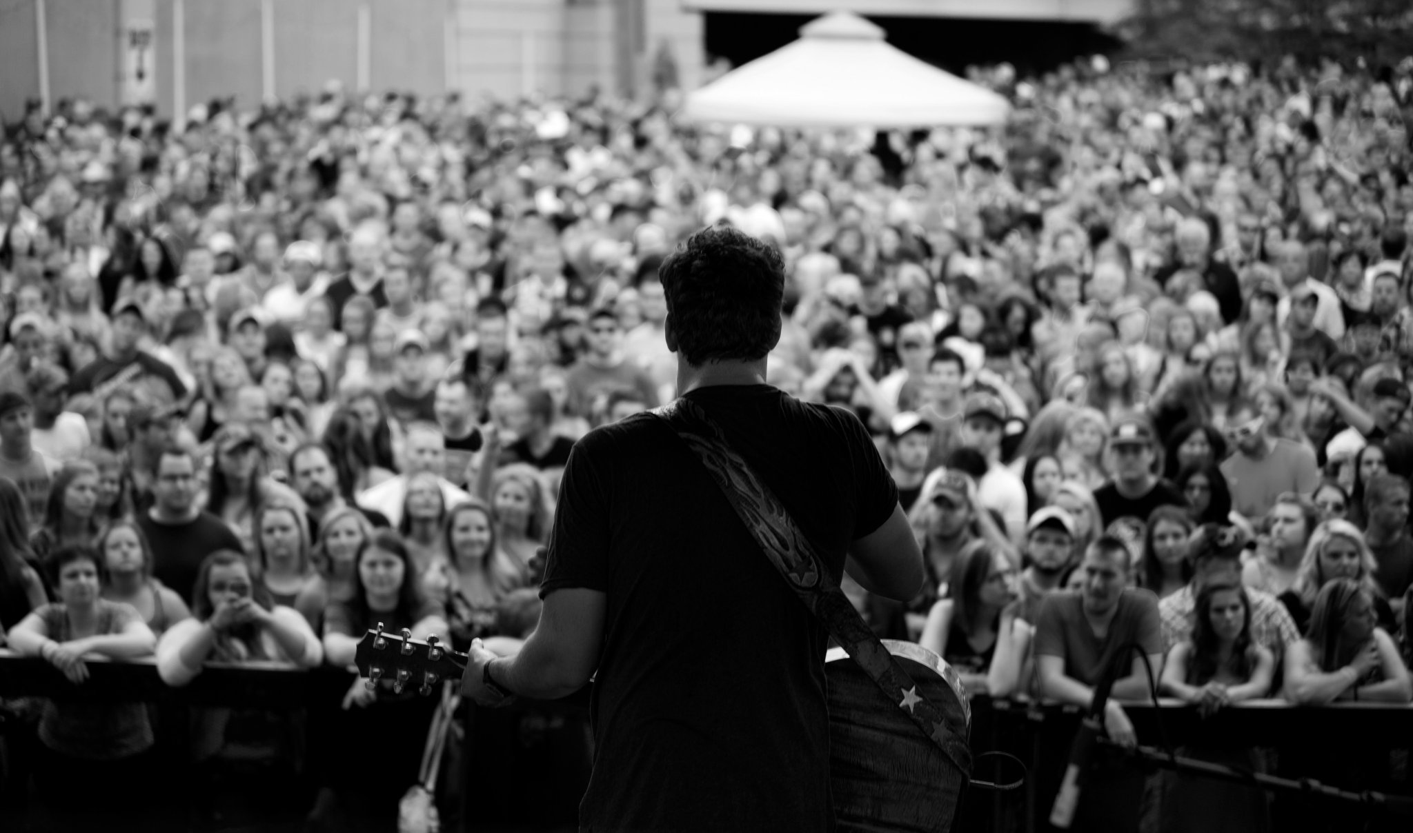 A musician with a guitar performing on stage in front of a large crowd at an outdoor concert.