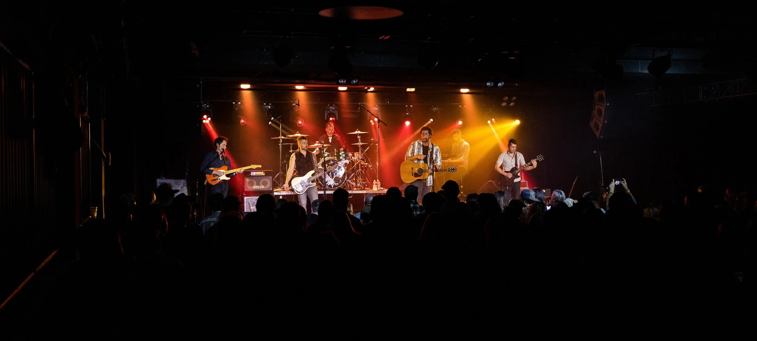 A live band performing on stage with colorful lighting and an audience watching.