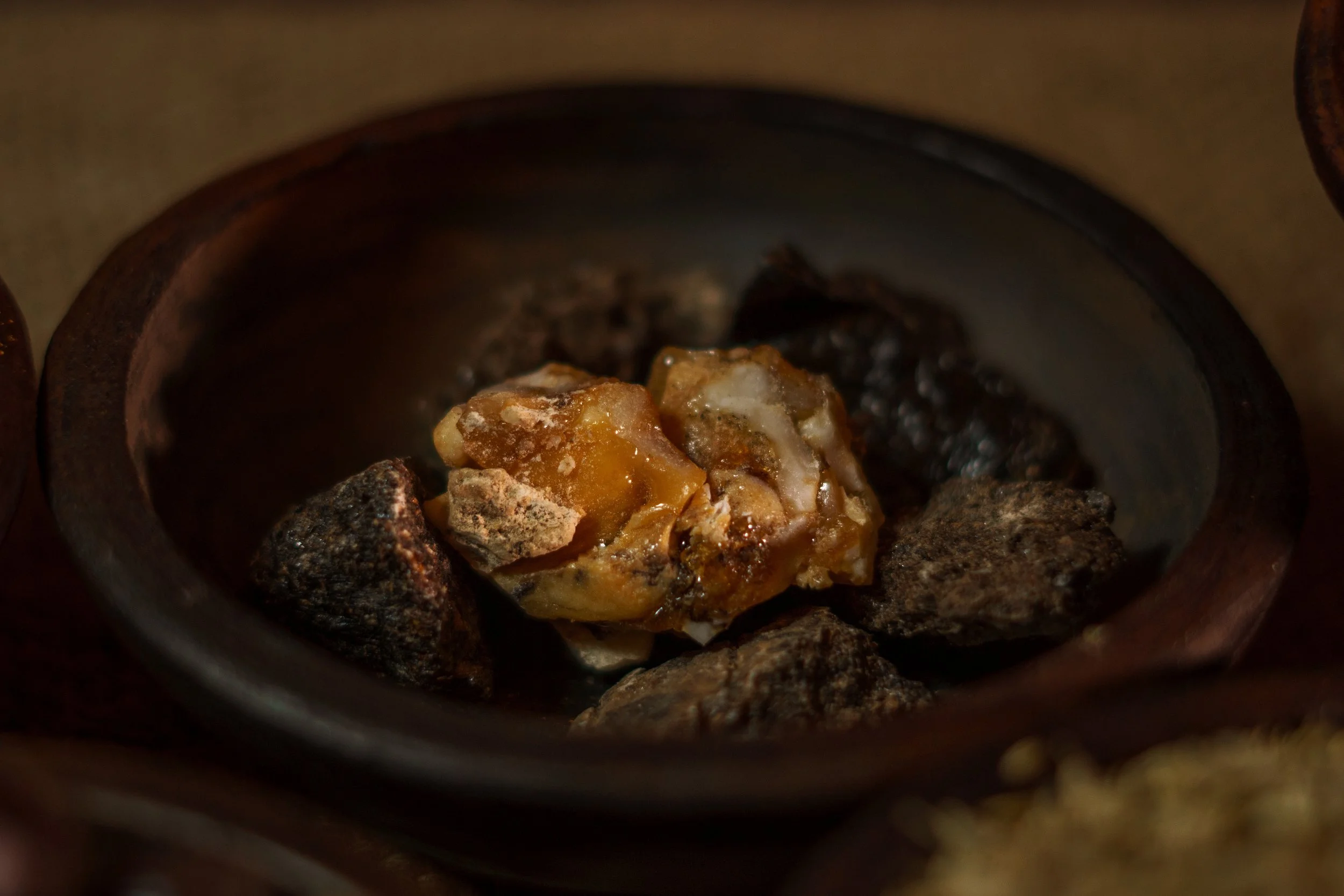 Close-up photo of a small piece of amber-colored resin surrounded by dark stones inside a container or vessel.