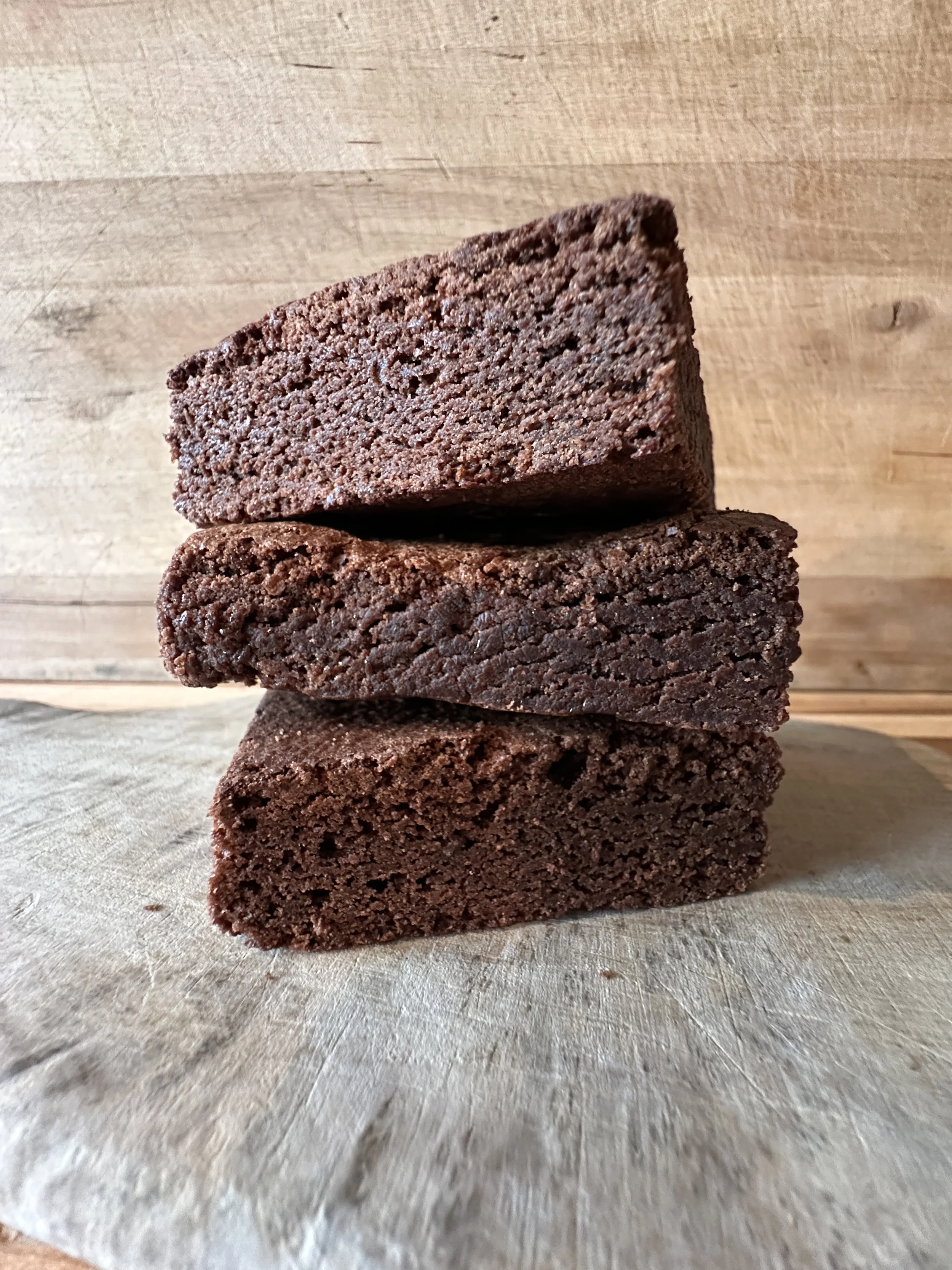 Three stacked chocolate brownies on a wooden surface with a wooden background.