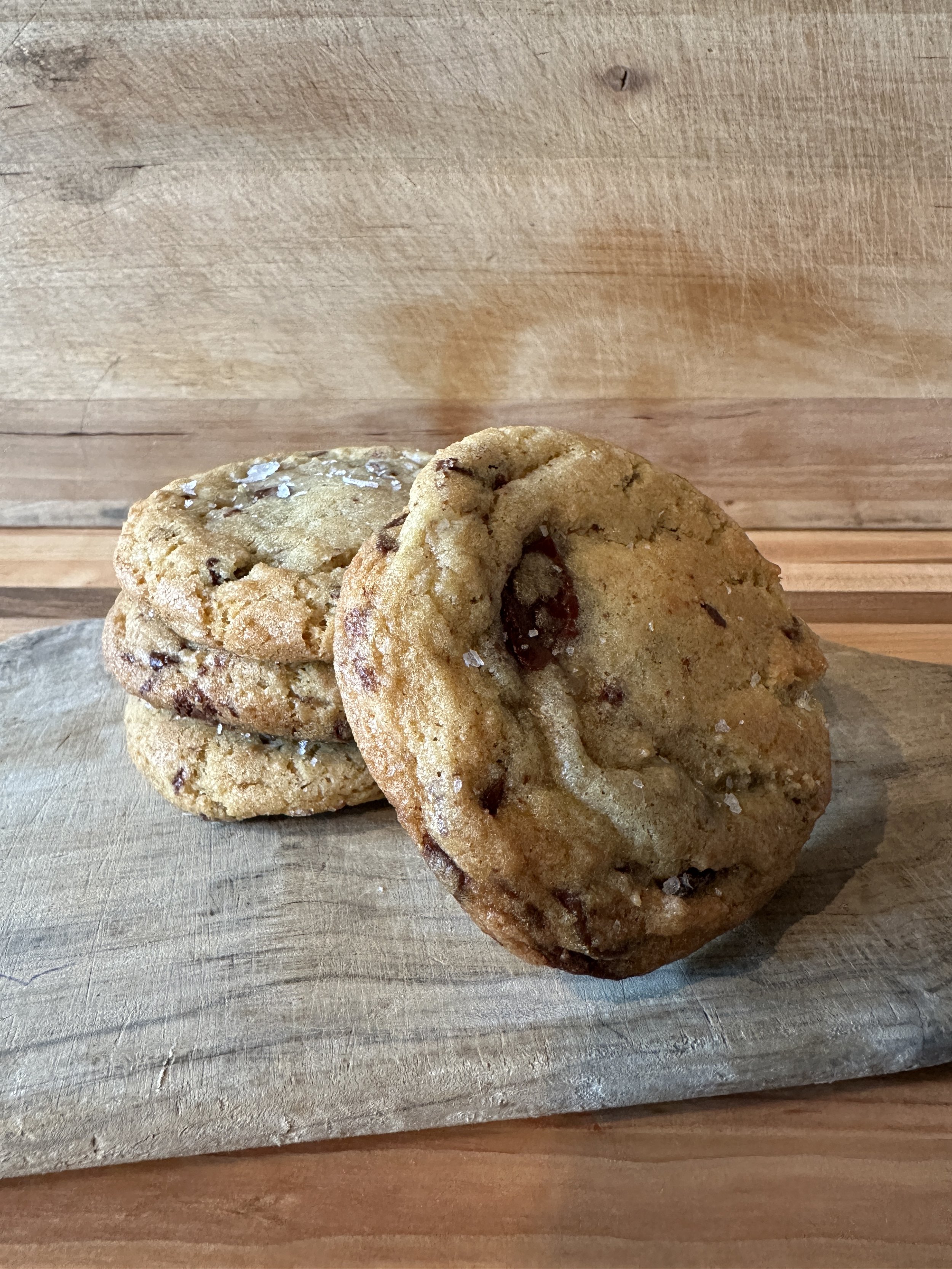 Three chocolate chip cookies stacked on a wooden serving board
