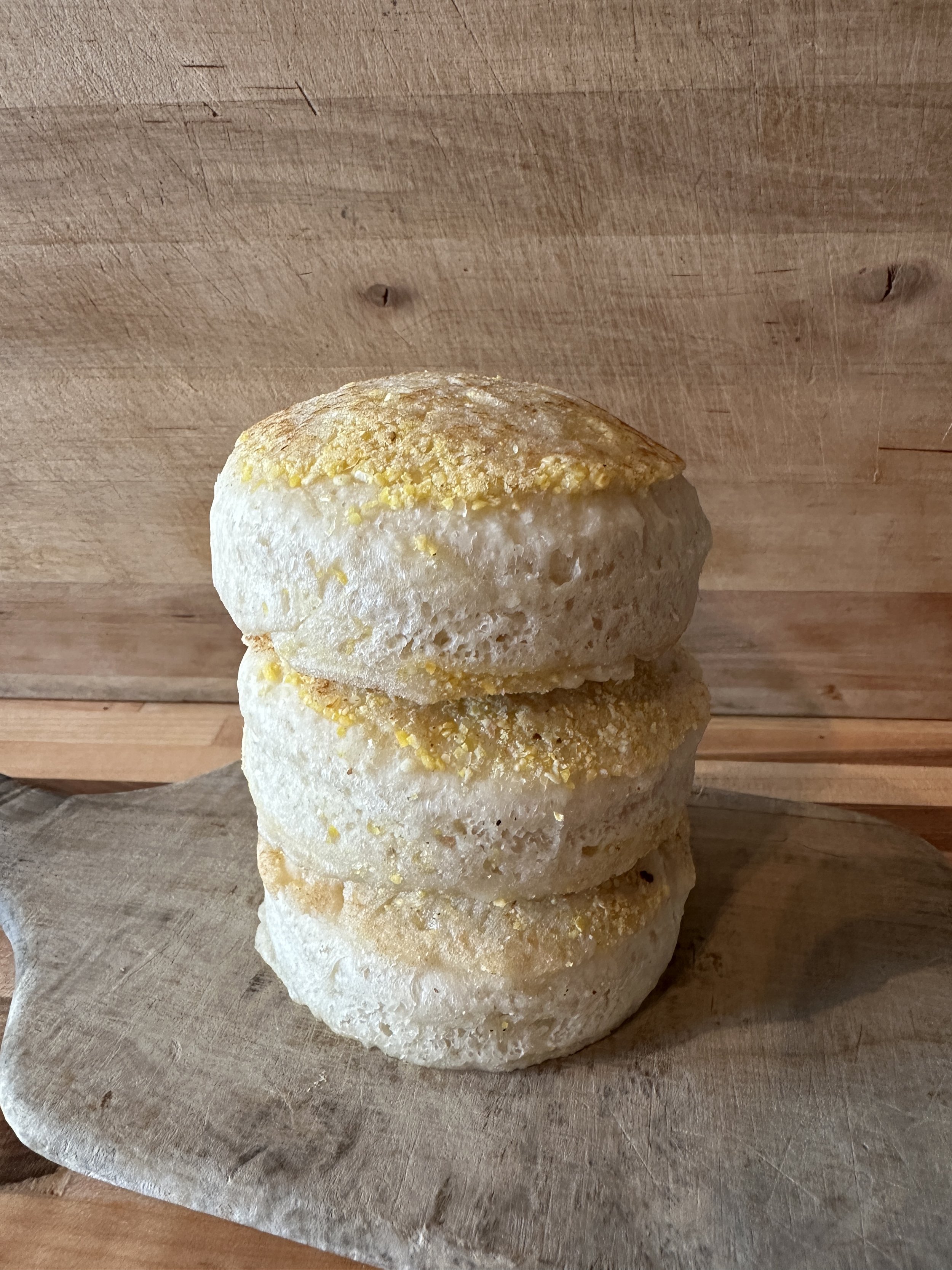 A stack of three lemon-flavored muffins with lemon zest on top, placed on a wooden serving board.