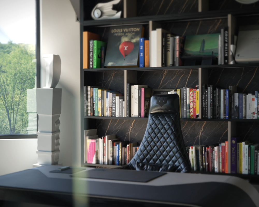 An office space with a black quilted leather chair, a bookshelf filled with books, a modern white sculpture, and a window showing greenery outside.
