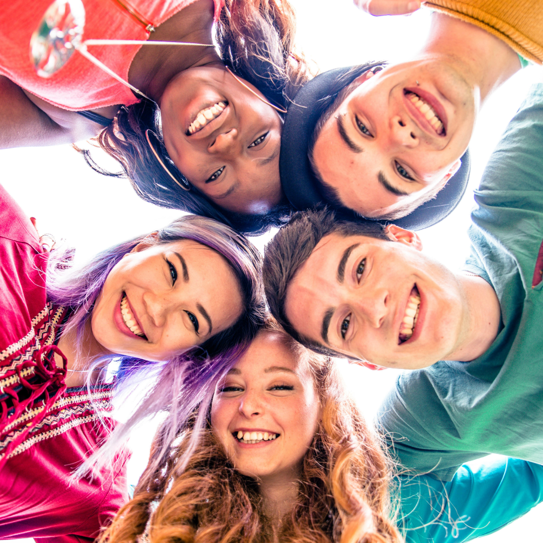 Group of five smiling young friends looking down at the camera in a circle.