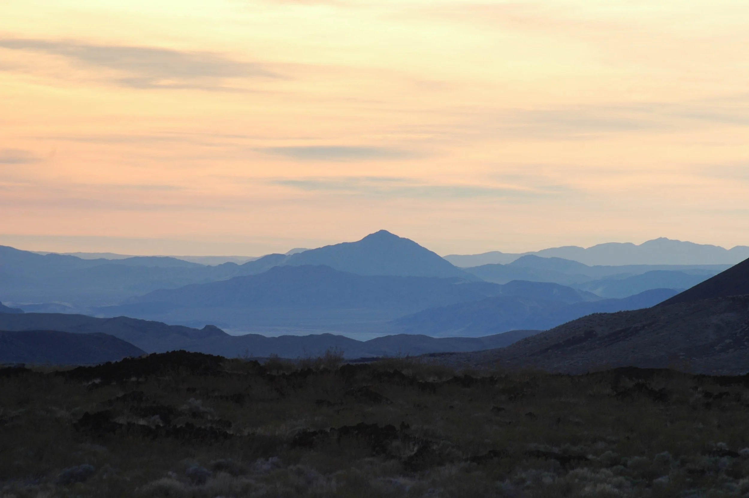 Scenic mountain landscape during sunset with layered mountain ranges and a pinkish-orange sky.
