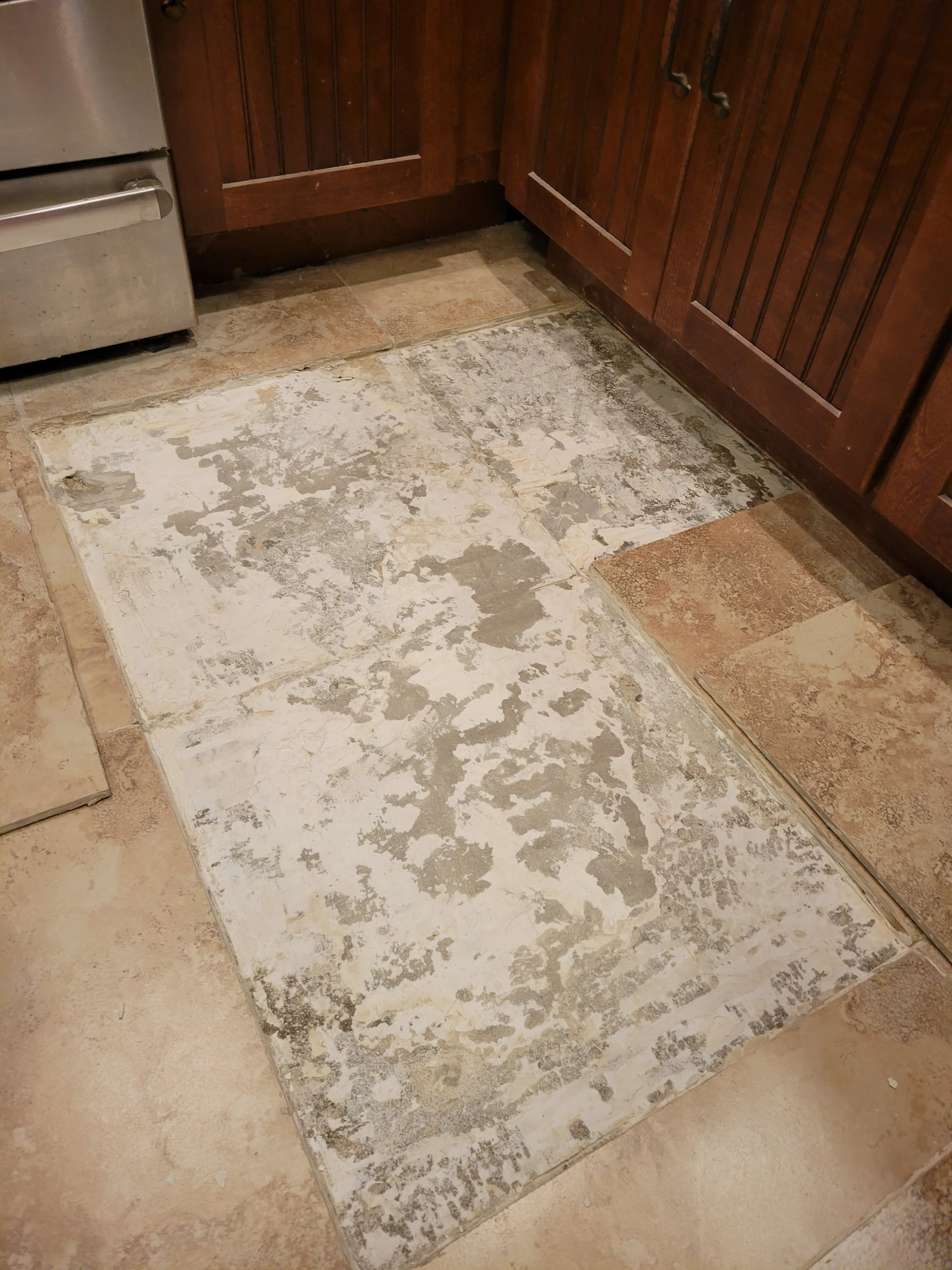 Kitchen floor with a large worn-out area where the tiles are damaged and missing, exposing the subfloor underneath.
