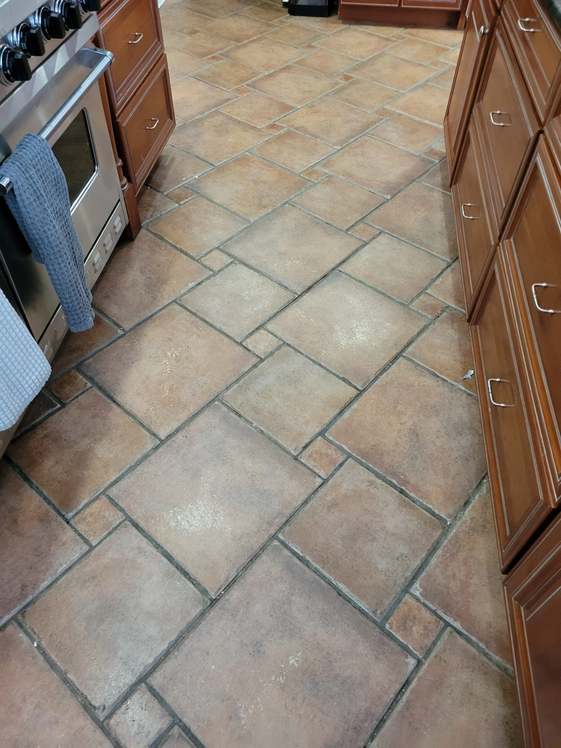 Kitchen floor with large brown and tan tile, dirty grout lines.