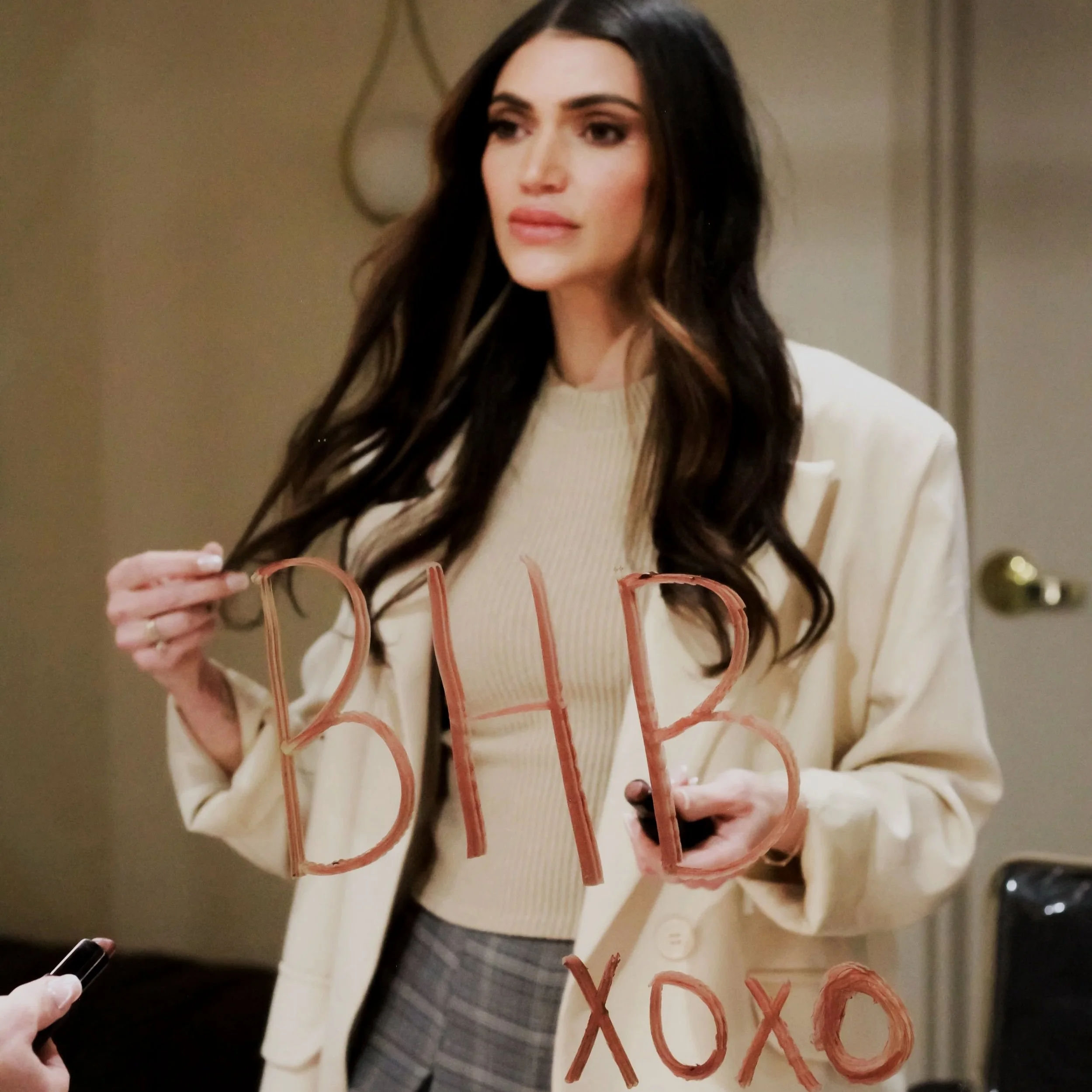 Woman with long dark hair standing in front of the mirror that reads xoxo, BHB