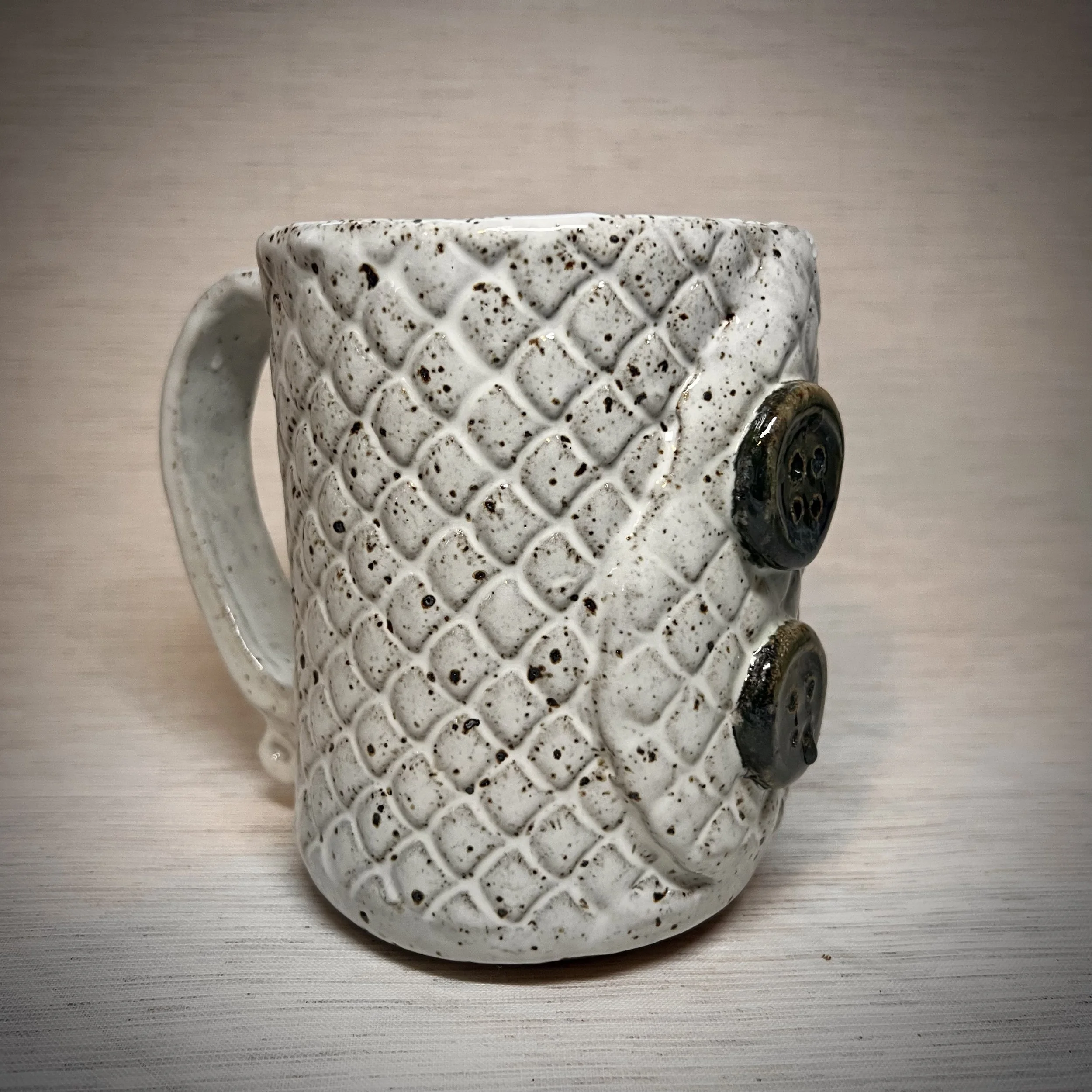 Ceramic mug with a textured pattern resembling a cozy sweater with buttons