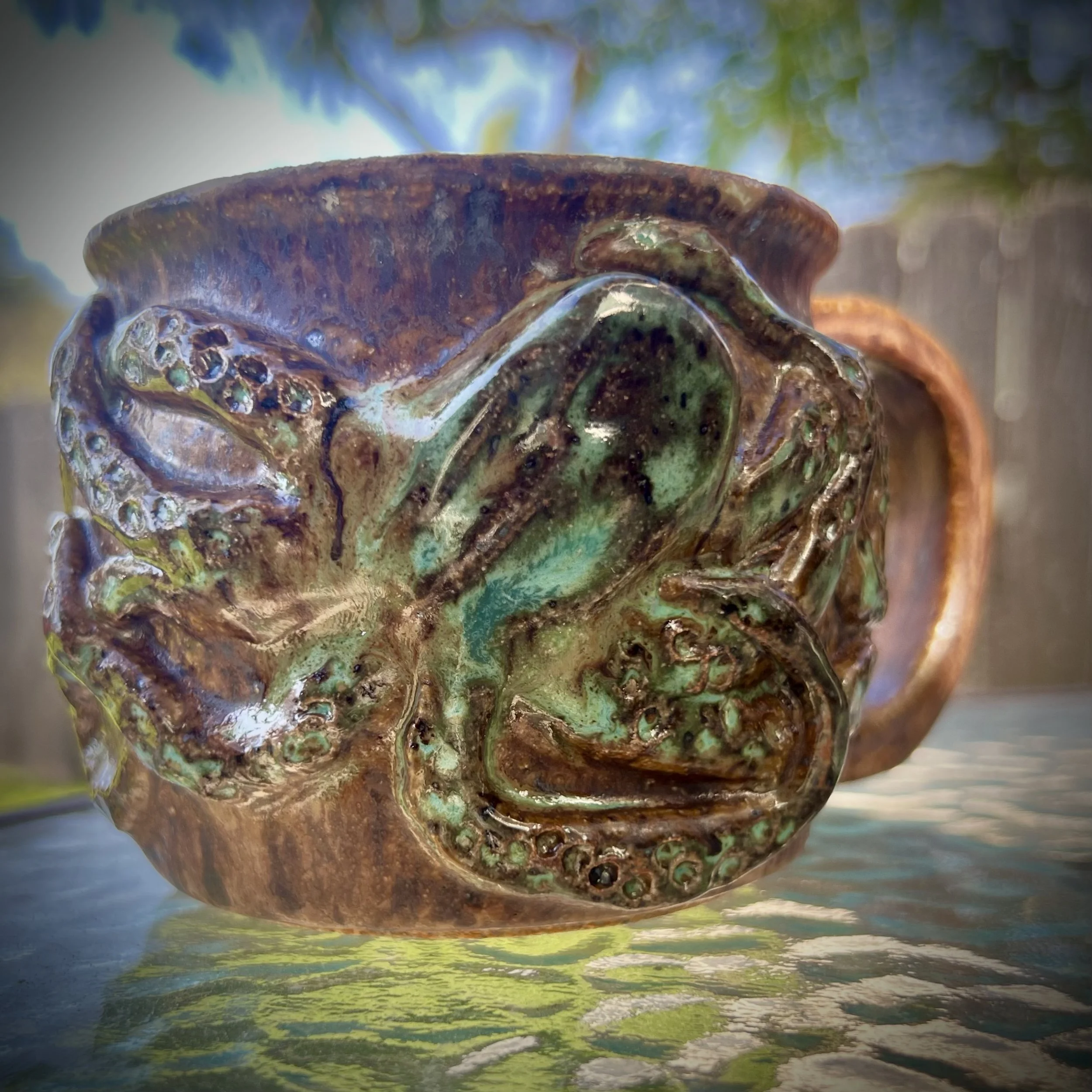 Close-up of a ceramic mug with a detailed octopus design, glaze in earthy tones with green accents.