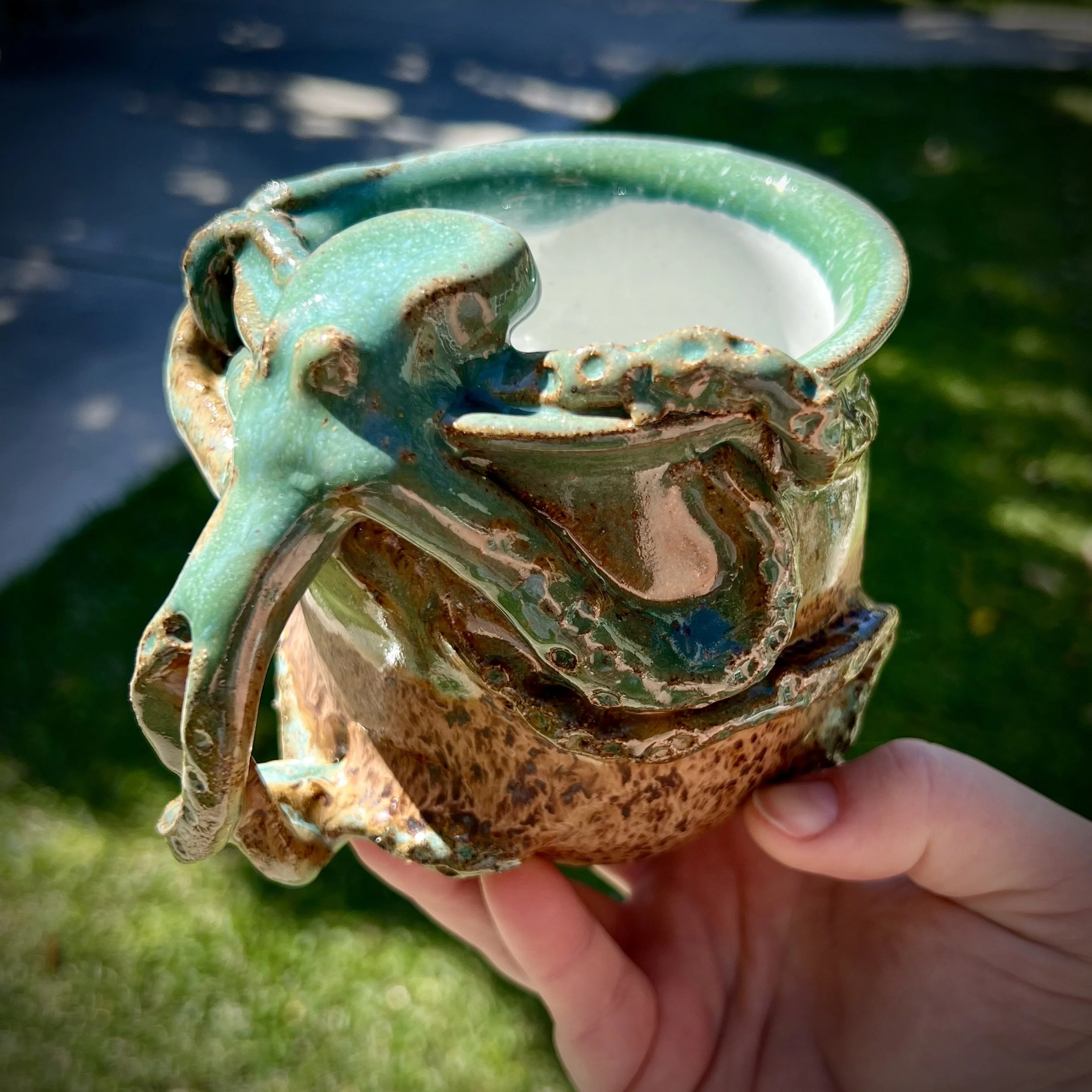 Hand holding a ceramic mug with an octopus wrapped around it.