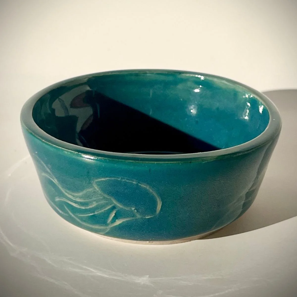 A ceramic bowl with a teal exterior and interior, hand etched with jellyfish.