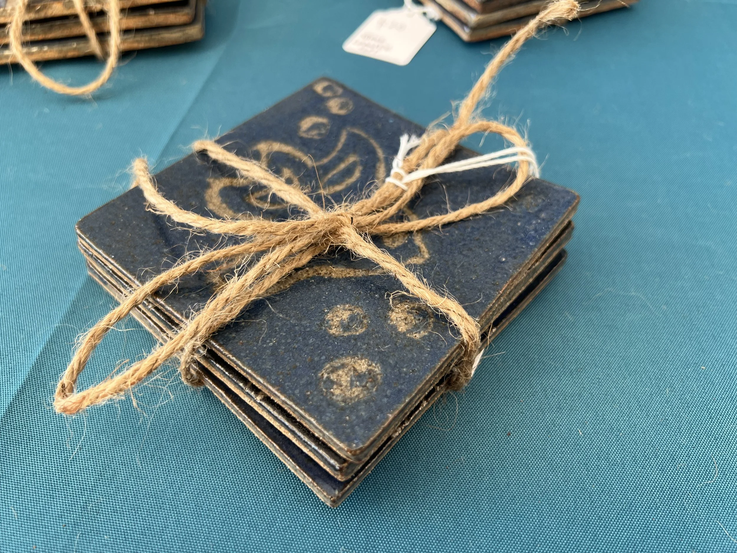 Stack of small black coasters with nautical designs, tied with a piece of tan twine.