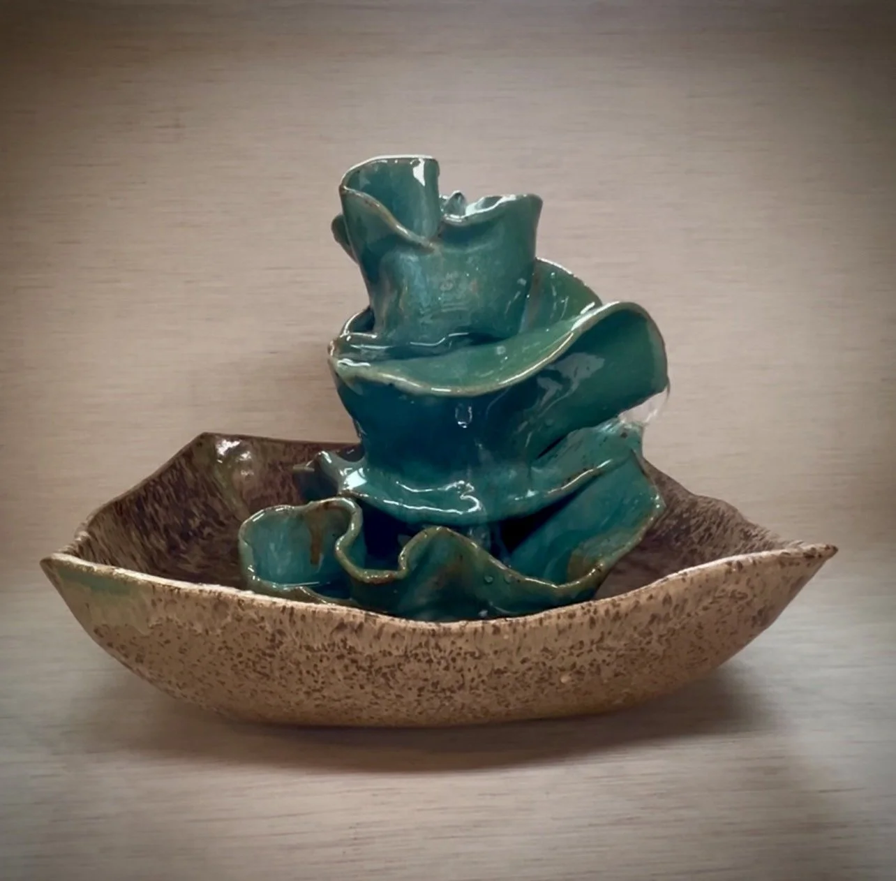 A ceramic sculpture of abstract turquoise and green shapes in a beige, textured bowl.