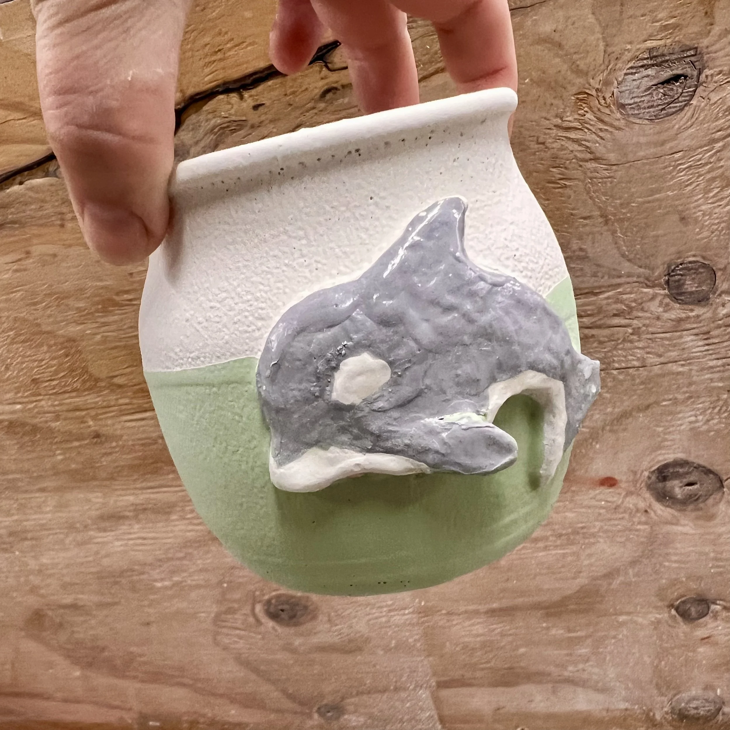 A ceramic pot with a raised, painted orca.