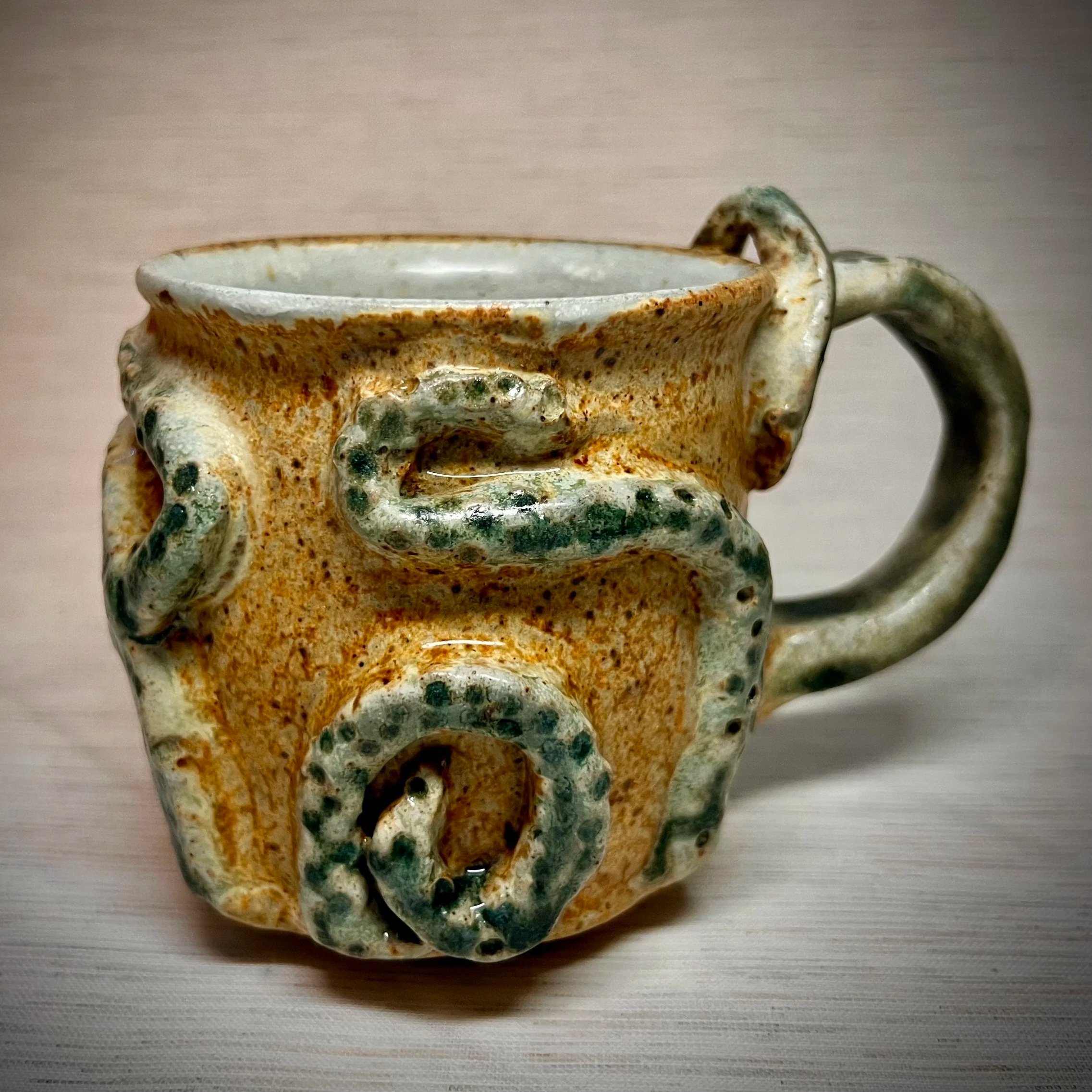 A ceramic mug with a textured surface and a handle, decorated with raised, swirling octopus design.