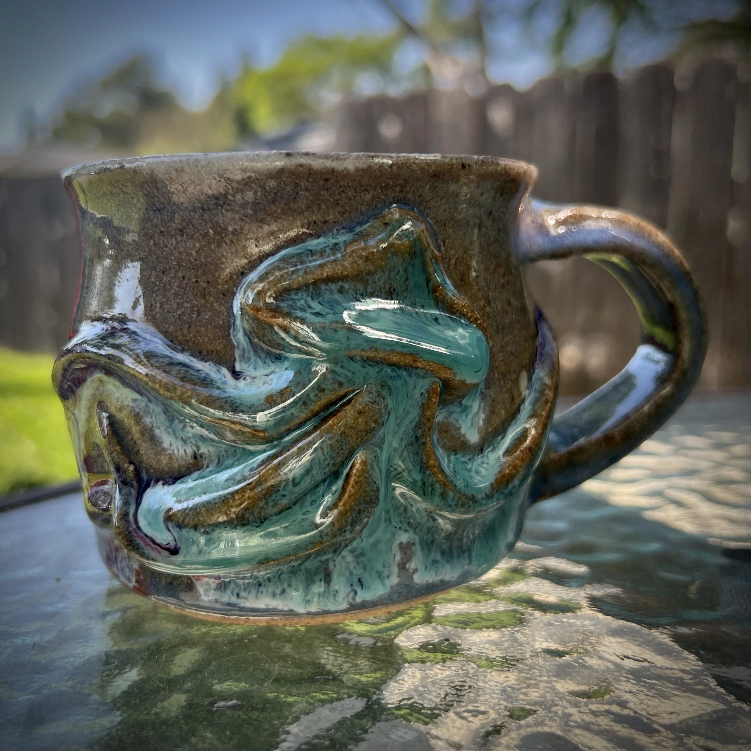 A ceramic mug with a textured brown exterior and a glossy, swirling turquoise-blue and jellyfish design.