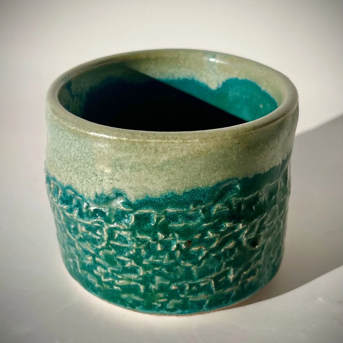 Ceramic cup with textured turquoise and green glaze.