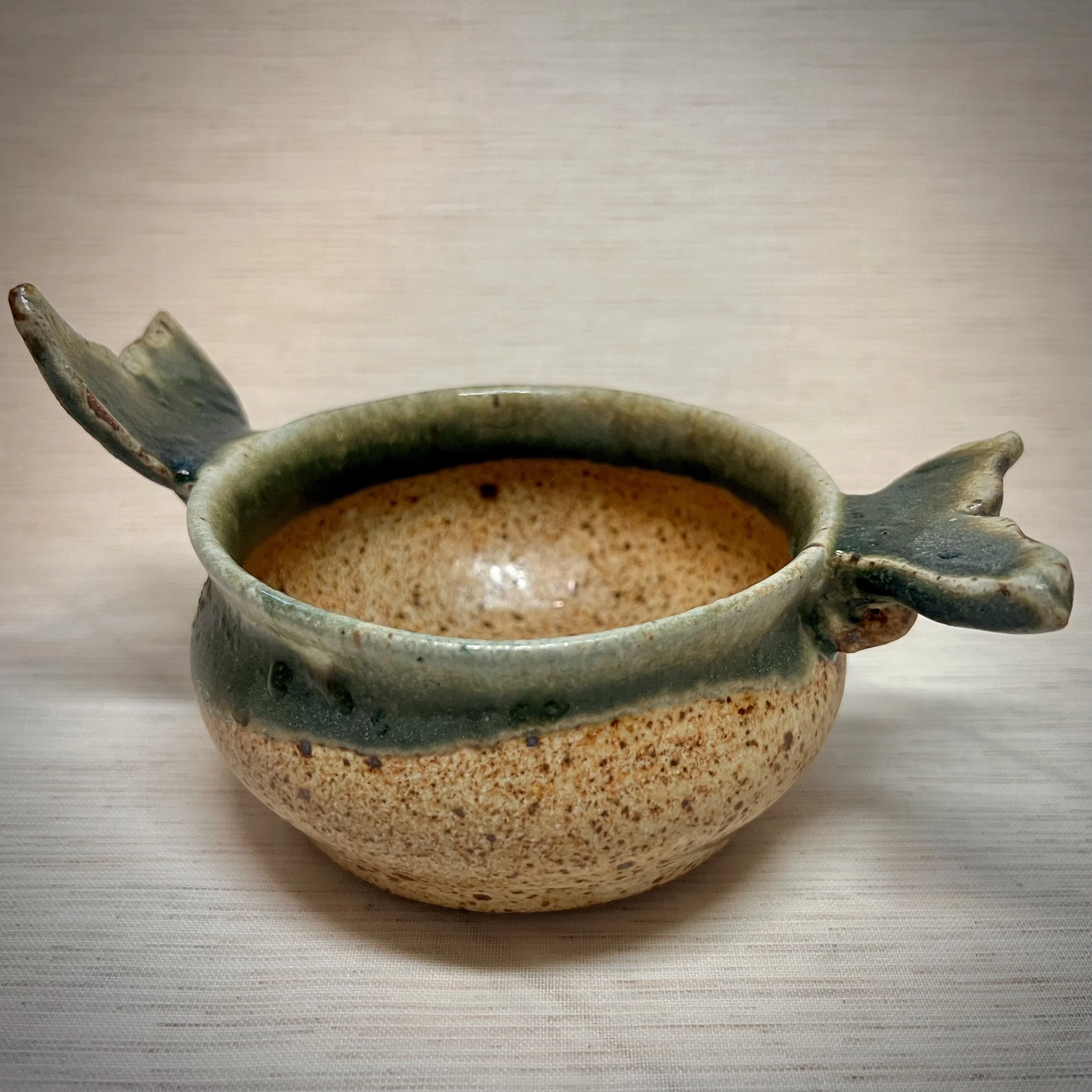 A ceramic bowl shaped like a fish with a round body, fish fins on the sides, and a fish tail on the back.