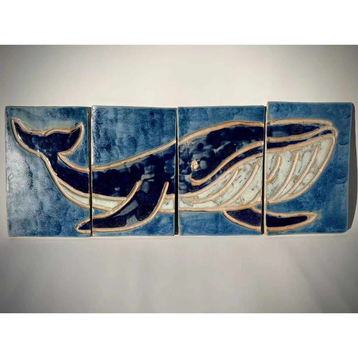 Ceramic wall art depicting a blue whale with a background of ocean waves.