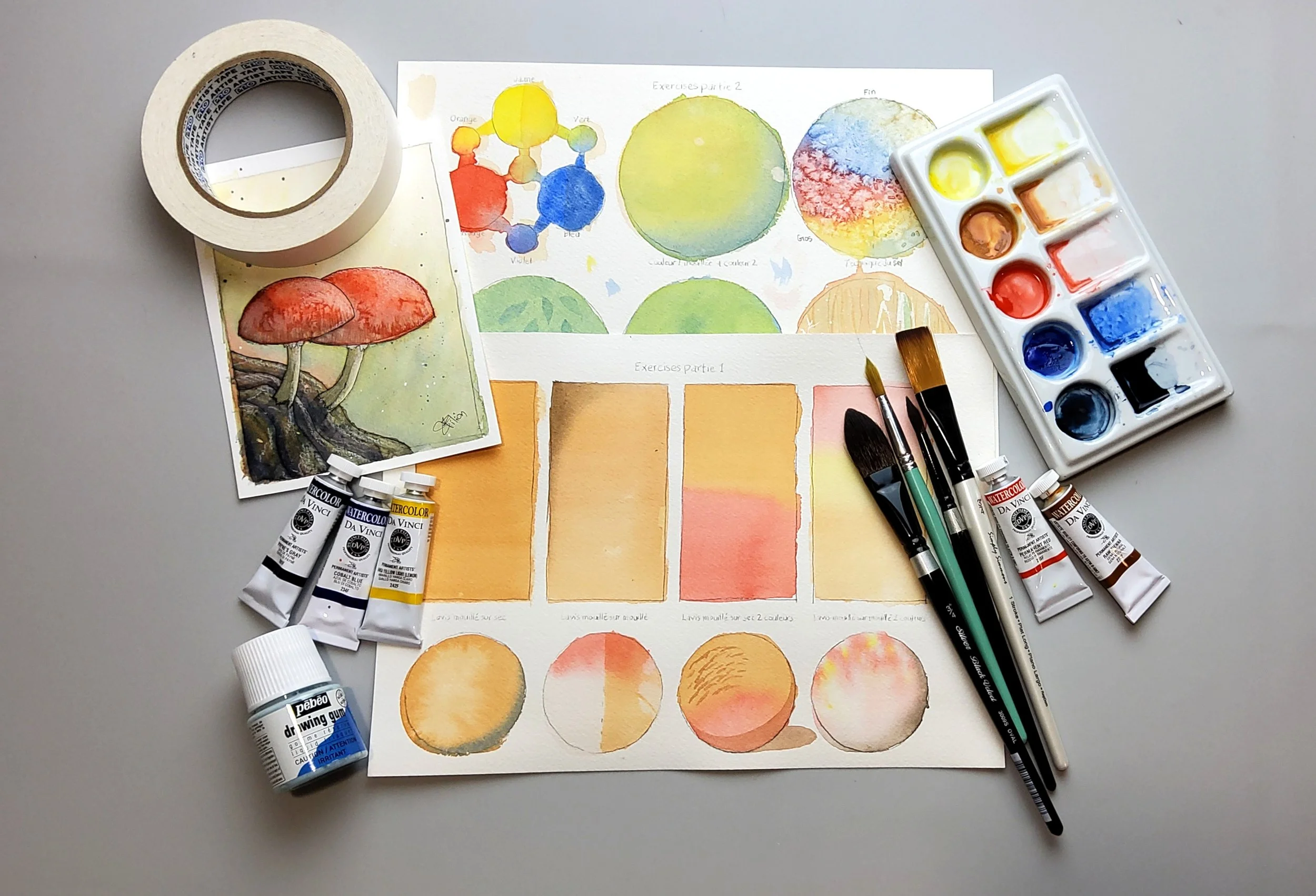 Matériel de peinture, pinceaux, tubes de peinture, aquarelle, peinture en palette, papiers avec exercices de peinture, pinceau rond, pinceau plat, masque pour peinture, sur une surface grise.