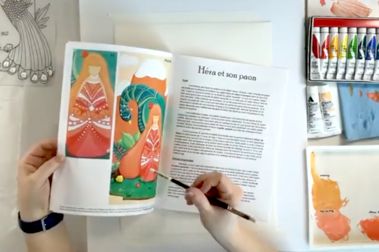 Une personne peint un paon en utilisant des peintures acryliques, avec d'autres illustrations et matériel artistique sur la table.