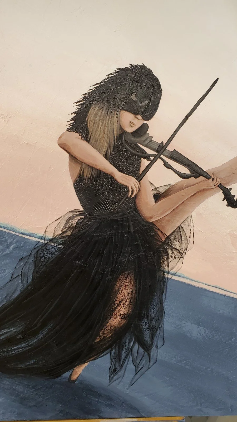 Une sculpture représentant une femme jouant du violon, vêtue d'une robe noire en tulle avec de détails en relief, ses cheveux longs et droits, debout sur un sol grisurry, contre un mur beige.