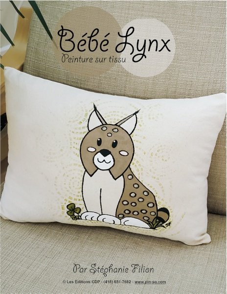 Coussin blanc avec une illustration d'un jeune cerf stylisé, petite feuille et texte en français. En arrière-plan, affiche avec le nom 'Bébé Lynx' et mention 'Peinture sur tissu'.