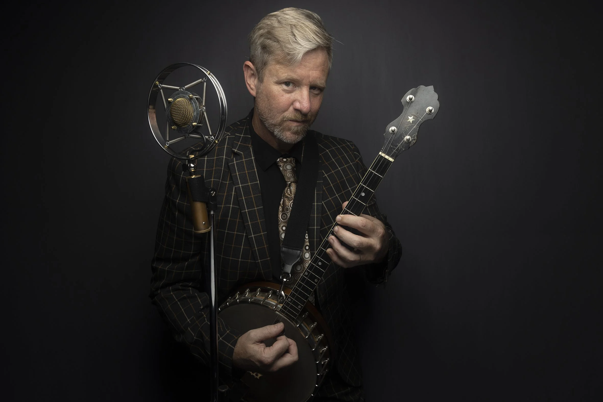 Guy Forsyth posing with a banjo beside a vintage microphone