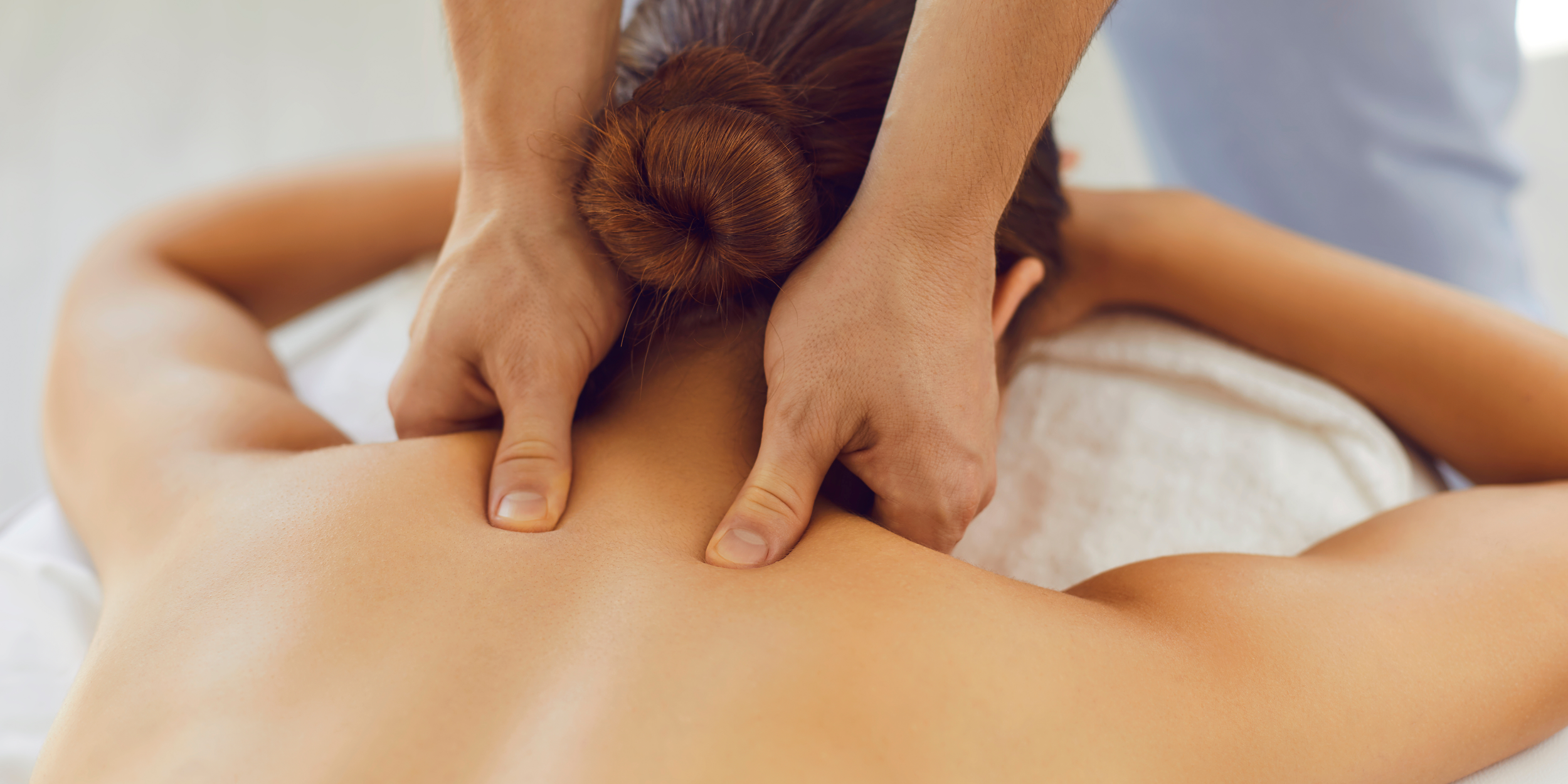 A person receiving a back massage with focus on the shoulder area, lying face down on a massage table.