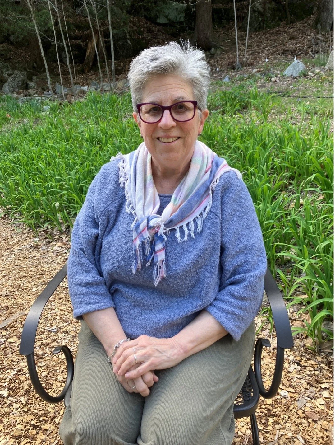 Lora Langston sitting in chair on garden path smiling