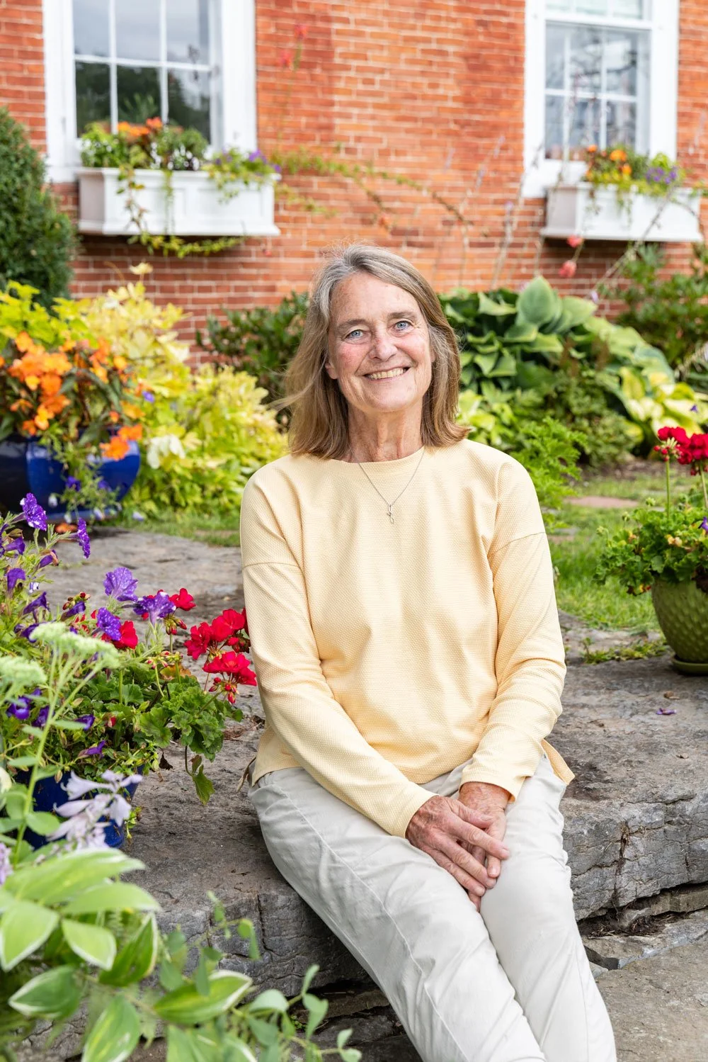 Patricia Troyan sitting on stone step next to flowers smiling