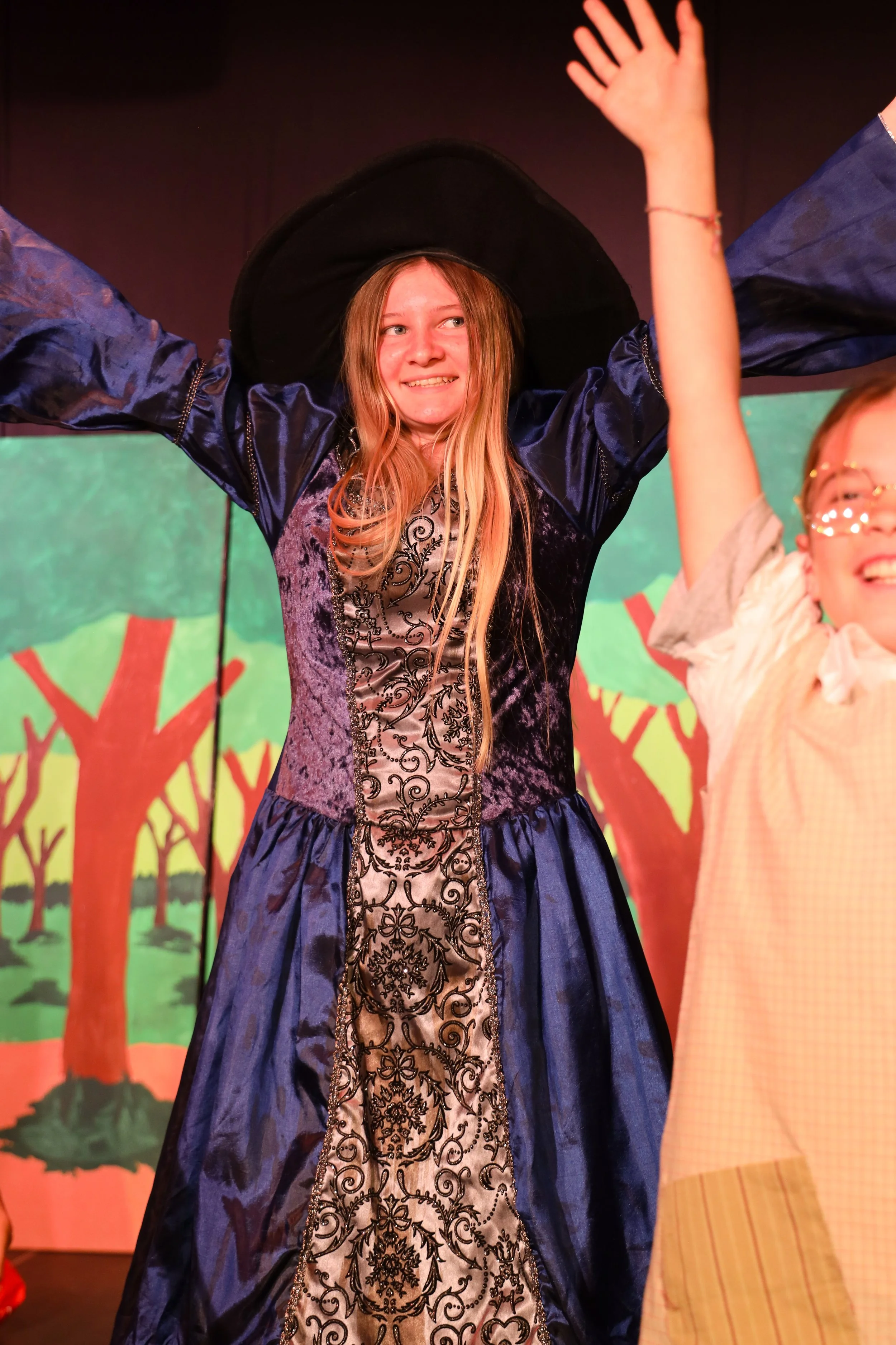 A person with long hair dancing on a stage while holding a microphone, with a black curtain in the background.
