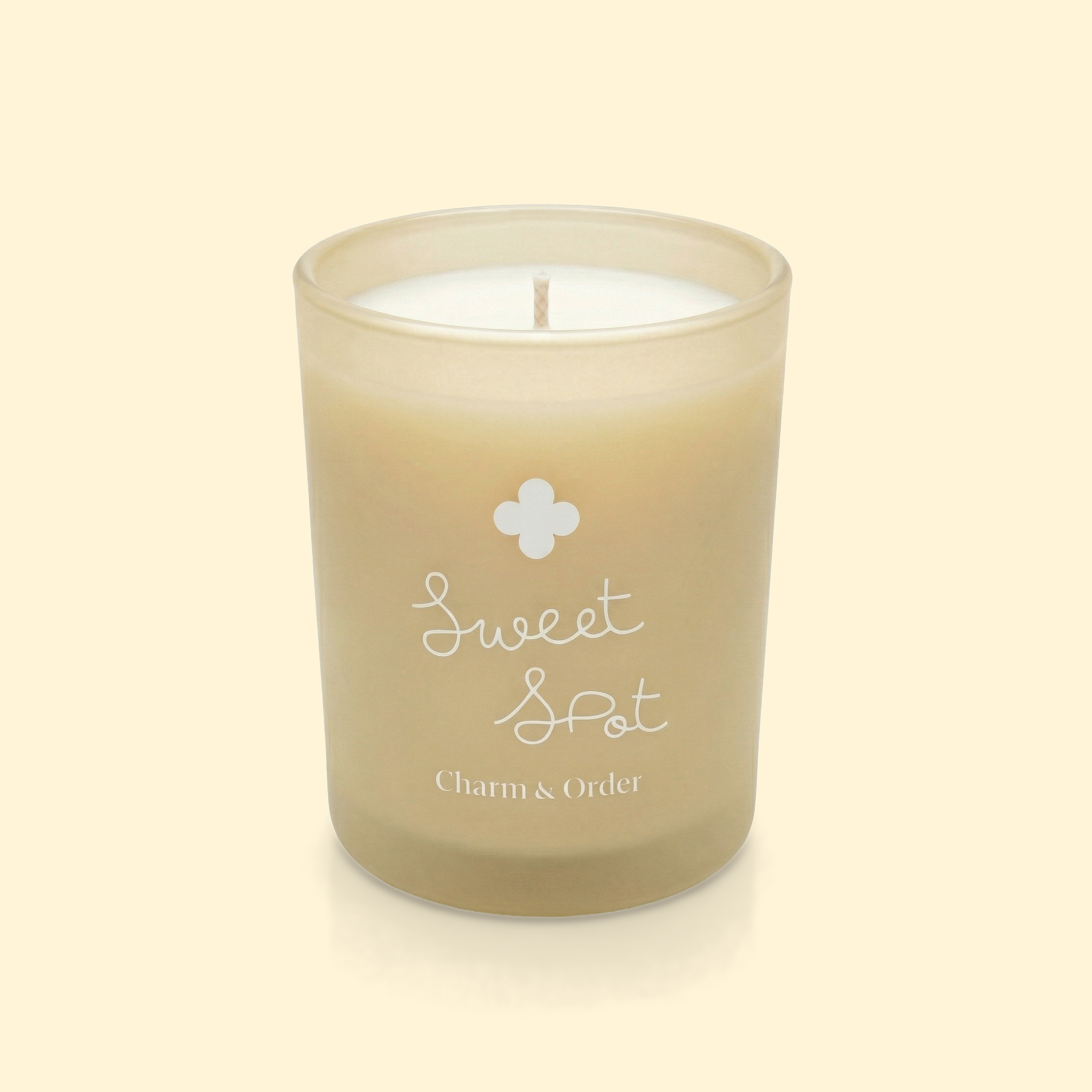 A beige candle in a container with the words 'Sweet & Set' and 'Charm & Order' printed on it, with a single wick at the center.