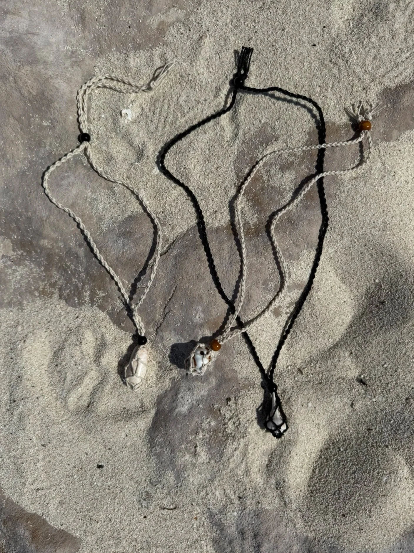 Three necklaces with shells and beads laid on sand.