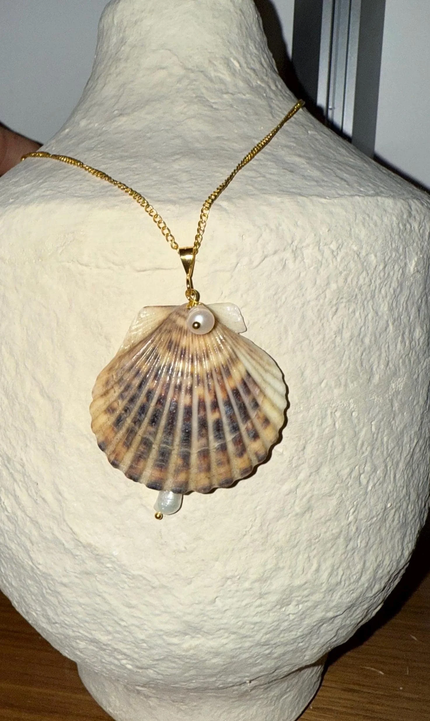 Gold necklace with a shell pendant and pearl accents on a white textured bust display.