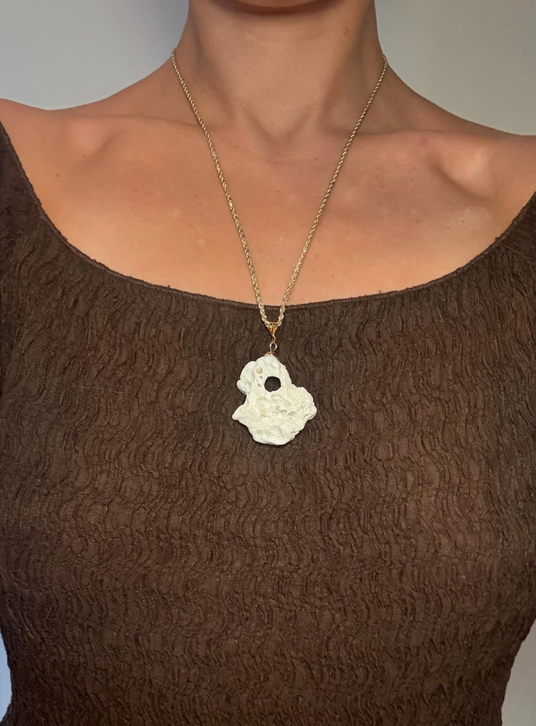 A person wearing a brown textured top and a gold chain necklace with a large irregularly shaped white pendant.