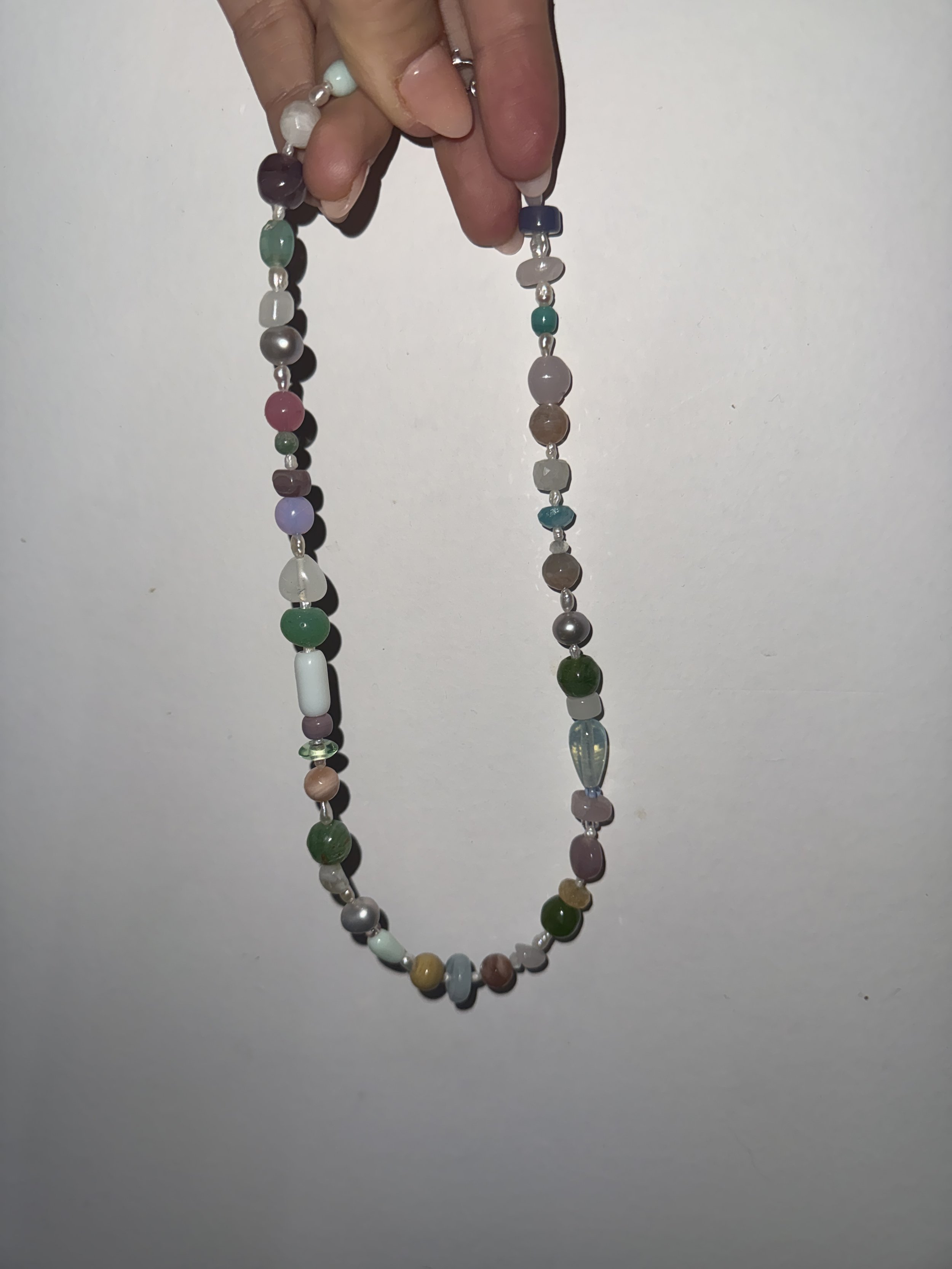 A hand holding a colorful beaded necklace with various shaped beads against a white background.