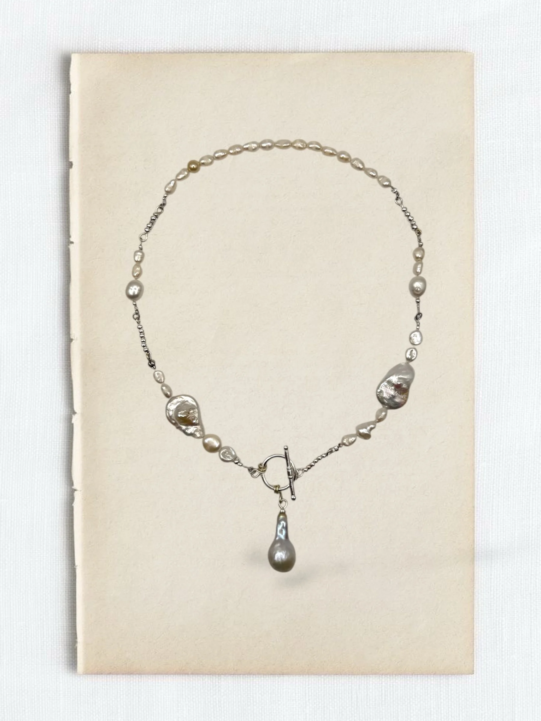Silver pearl and stone necklace with a large hanging pearl pendant displayed on a cream background.