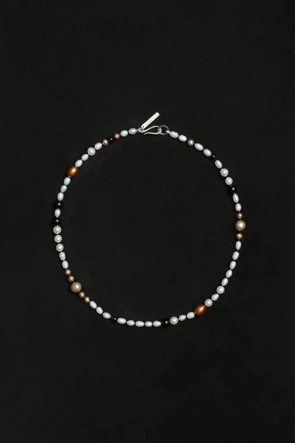 A pearl necklace with alternating white, brown, and reddish-brown pearls on a black background.