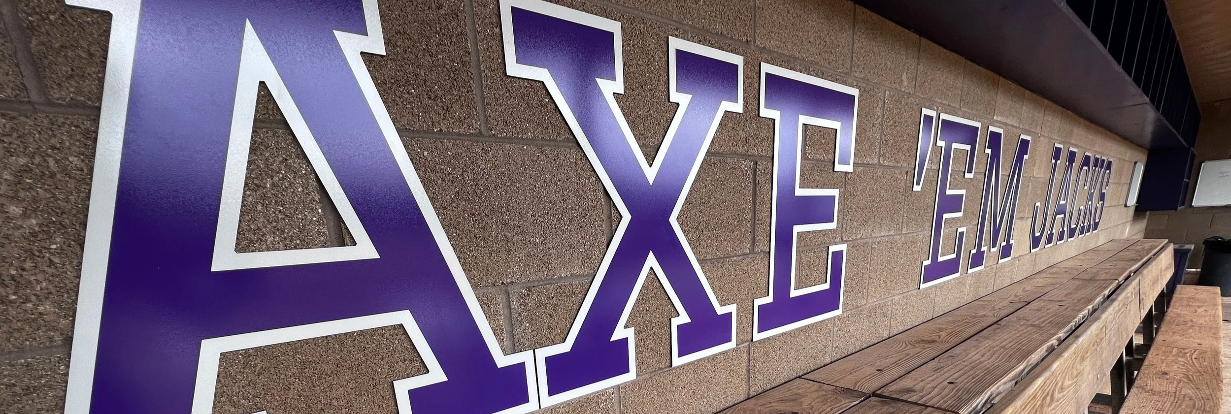 Large purple and white Greek letters spelling 'AXE' on a brick wall.
