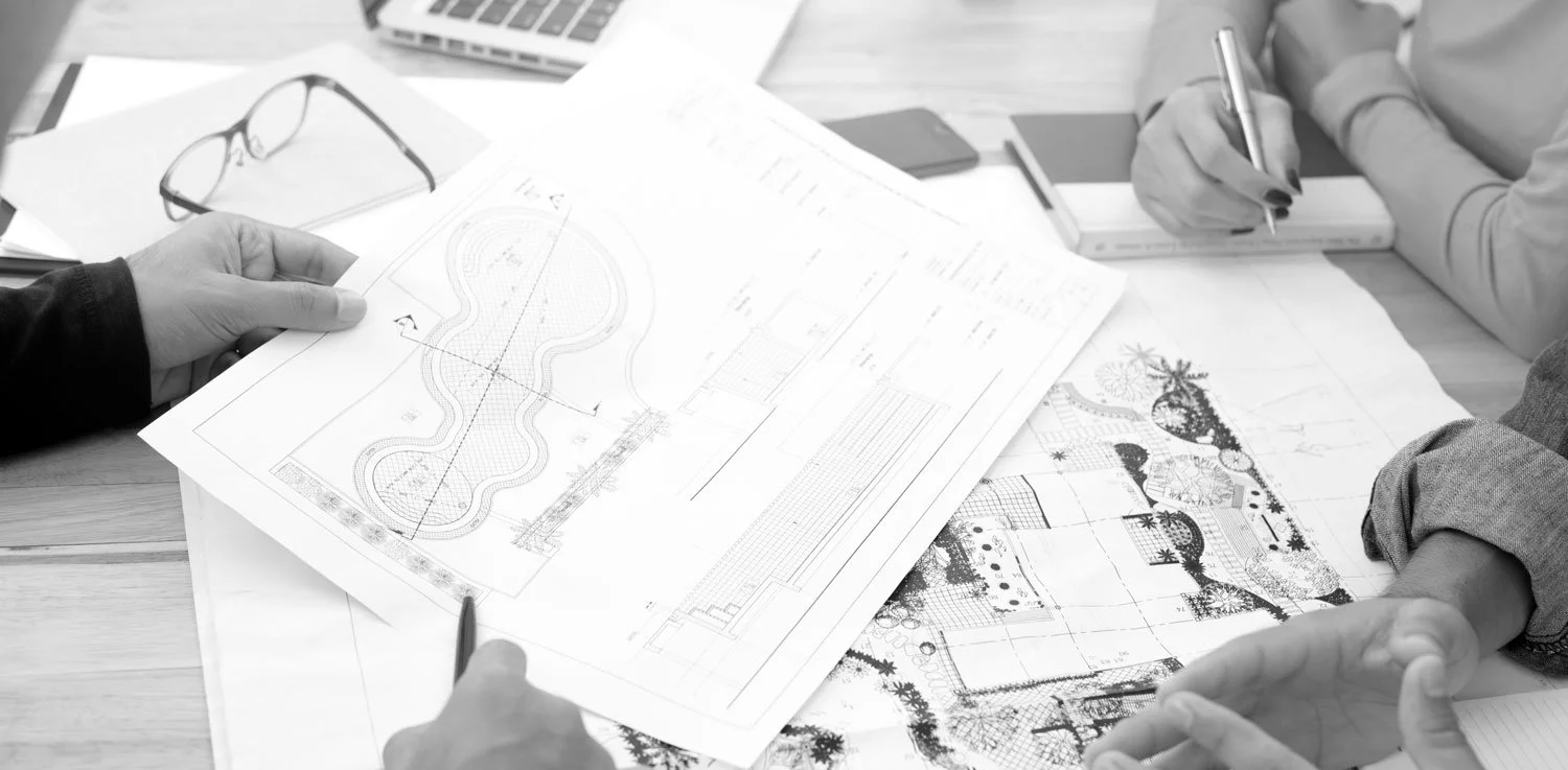 People reviewing landscape design plans and blueprints on a desk with gardening sketches and measurement tools.