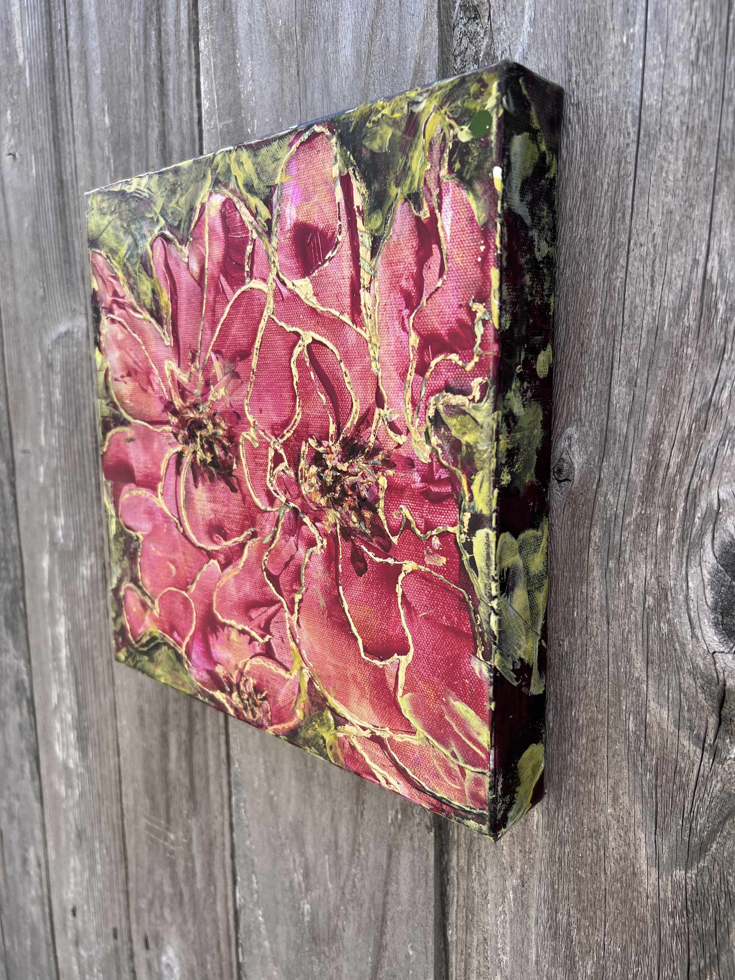 Textured pink floral painting with gold leaf accents on a 10×10 canvas, featuring bold petals and expressive abstract detail.